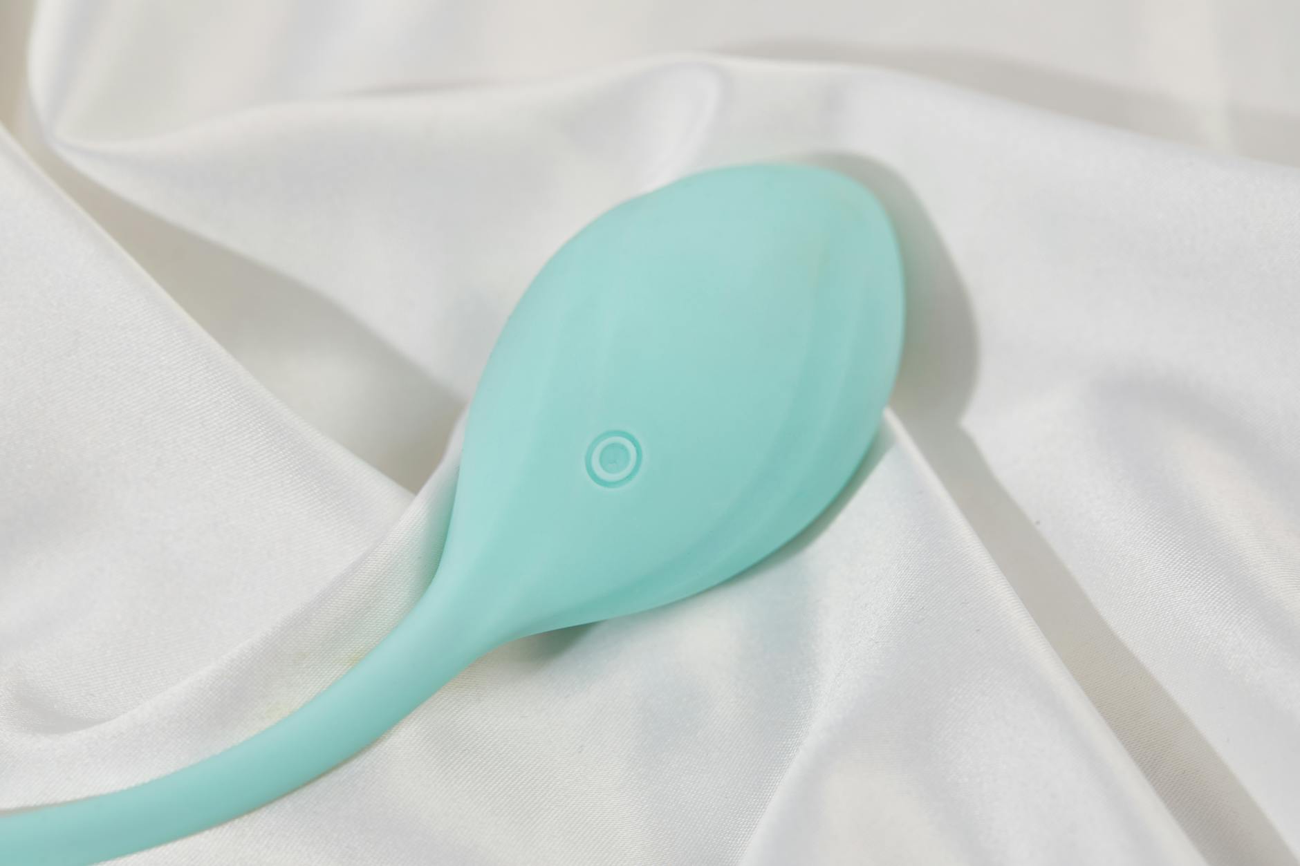A hand holding a blue vibrator above a decorative glass bowl on a neutral surface