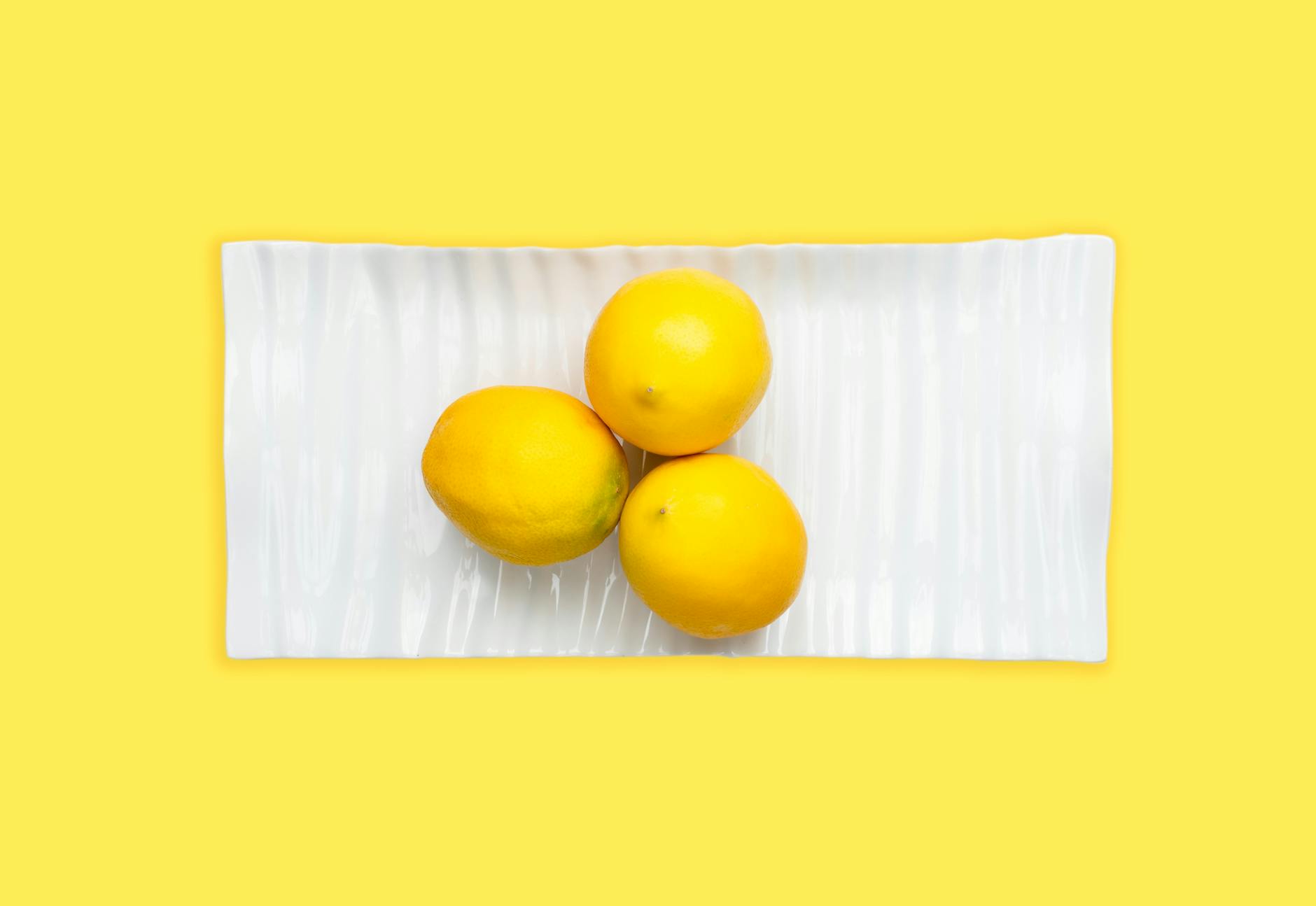 Three fresh lemons on a white plate with yellow background, representing clarity and fresh beginnings