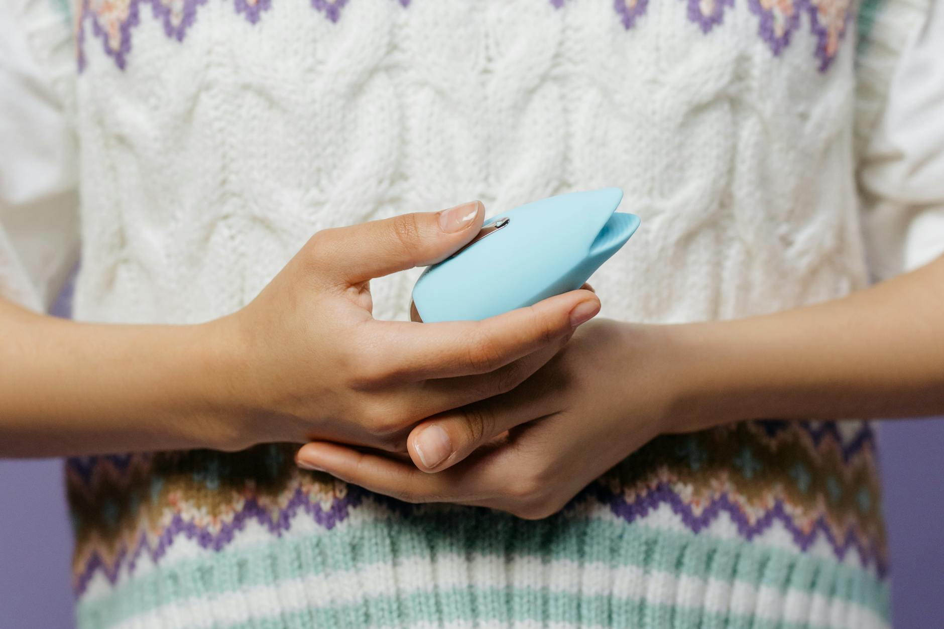 Woman holding blue personal massager against a knitted sweater.